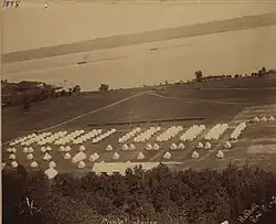 Black-and-white photo showing rows of tents on shore of lake