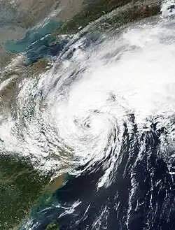 A photograph of a weakening, but still strong, tropical storm over the northwestern Pacific Ocean. Although its circulation is still tightly-wound, convection is light on the southern side, mostly limited to cloudiness and rain showers. By contrast, there is an extensive area of deep convection to the north and northeast of the storm, with streaks of high, wispy clouds emanating from the northern edge of the convection. To the west of the storm is an area of puffy, parallel clouds that are indicative of cooler weather; this is a hint that the storm is in the process of transitioning into an extratropical cyclone.