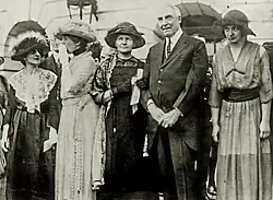 Harding stands beside Marie Curie. Curie has her arm around Harding's. Others stand around them.