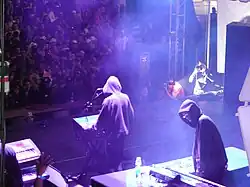 A man in hoodie with electronic musical instruments performing at an annual electronic dance music event.
