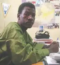 Kaka, a man with short hair, sitting at a desk holding a pen and wearing a green shirt