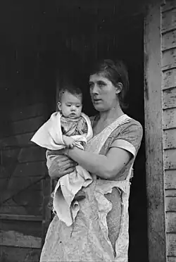 A woman holding a baby during the Great Depression. They are standing right outside of their house in Shannon City.