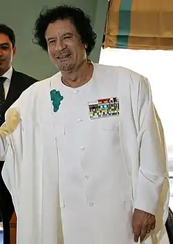A middle-aged man, with black hair and facial stubble, wearing a white robe.
