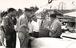 Group of men standing, in uniform or suit on an air base