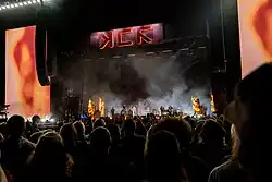 My Chemical Romance performing on the stage depicted earlier, now on fire with smoke covering the arena.