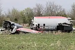 A destroyed gray and red aircraft fuselage and tail in a field