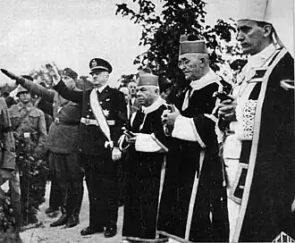 three priests and several saluting males in military uniform