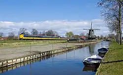 An NS Intercity passes the windmill due to its proximity to the Bovenkarspel Flora railway station (2015)