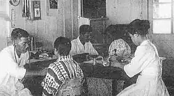 Two Japanese physicians auscultating seated patients while a Japanese nurse writes at a desk