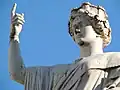 Top of a white statue, showing the head and an arm, a finger pointing to the sky.