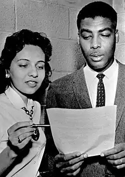 A man and woman look over a document the man is holding. The woman points to a particular section with a pen.