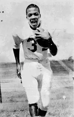 Nemiah Wilson, pictured in motion running towards the camera holding a football wearing a jersey with the number 32.