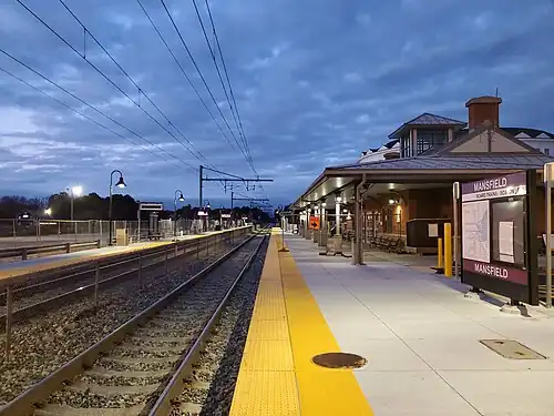 A railway station with two tracks and two side platforms seen in twilight. On the right platform is a modern station building.