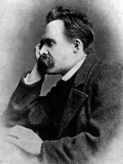 Black-and-white photo showing a man with a thick mustache from the side, wearing a dark suit and resting his head on his hand