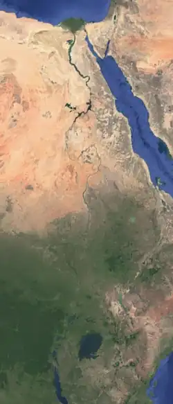 A photograph of the northeast Africa, taken from space. The Nile River is visible as a meandering blue line, running vertically. The river starts at the bottom in green forested area, and goes upward through an orange-yellow desert, then ends in a blue sea at the top.
