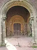 Doorway without wrought iron hinges on door and dogs tooth pattern around archway.