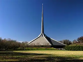 The North Christian Church's spire as seen from across a field. The base of the church has a sloped roof supporting the spire, which tapers as it rises.