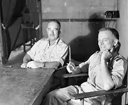 Two men in light-coloured uniforms seated at a table