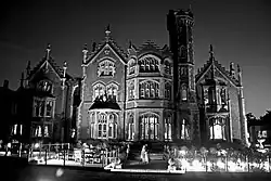 Large Gothic Revival mansion at night with ornate windows and central tower, dramatically lit against a dark sky.