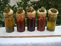 Five shot glasses of different coloured sauces, with a panipuri placed atop each.