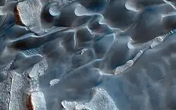 Closeup, color-enhanced image of Olympia Undae dunes with melting/subliming ice-cap fragments. Note Barchan dunes and patterned ground. Width of image is about 1&nbsp;km/3000&nbsp;ft.