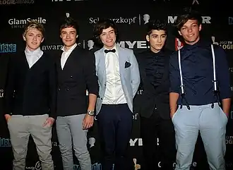 Five teenage boys wearing formal clothes standing next to each other and posing on a red carpet at the Logie Awards. From left to right: Niall Horan, Liam Payne, Harry Styles, Zayn Malik, and Louis Tomlinson.