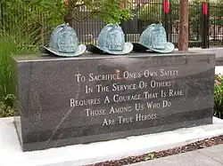 Three bronze helmets on top of a marble base reading "To sacrifice one's own safety in the service of other is rare. Those among us who do are true heroes."