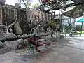 Orangutan on bench in jungle-themed indoor exhibit with waterfall and parrots.