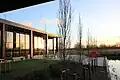 A photo showing the outside of the David Kato hub overlooking the pond. The photo was taken at sunset on a January afternoon, the sun is reflecting in the glass of the hub with contrasting black metal pillars