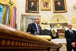 Apple Inc. CEO Tim Cook and Donald Trump in the oval office with a gold gift to the president in the foreground at the announcement of a $100 billion "investment" in the US