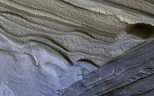 Image 7 Climate of Mars Photograph credit: NASA / JPL–Caltech / University of Arizona Although Mars is smaller than the Earth and 50 percent farther from the Sun, its climate has important similarities with the Earth, such as the presence of polar ice caps, seasonal changes and observable weather patterns. This image shows layered deposits in Planum Boreum, in the north polar region of Mars, which formed from a 3-kilometre-thick (2 mi) stack of dusty water-ice layers about 1,000 km (600 mi) across. The layers record information about the climate of the planet stretching back several million years. Erosion has created scarps and troughs that expose the layering. The tan-colored layers are the dusty water ice of the polar layered deposits, however a section of bluish layers is visible below them. These bluish layers contain sand-sized rock fragments that likely formed a large polar dunefield before the overlying dusty ice was deposited. This photograph, depicting an area approximately 1.3 km (0.8 mi) across, was captured by the HiRISE camera on board NASA's Mars Reconnaissance Orbiter. More selected pictures