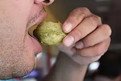 A person holds a panipuri between his fingers and puts it into his mouth.