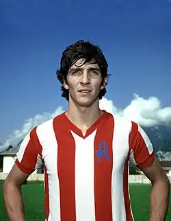 A standing man wearing a red and white sports shirt