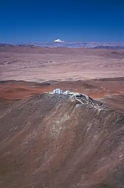 A snow-covered cone rises in the background above a hilly landscape with a building complex in the middle