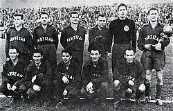 Black and white photograph of a football team. The player standing on the right, the captain, holds a trophy