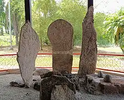 A cluster of stones dominated by three prominent vertical stones, of which the left and right have obvious carvings