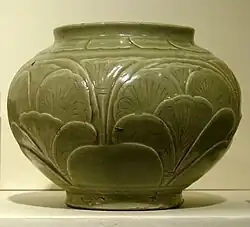 A green-grey bowl with a small bottom, a very wide center, and a top opening wider than the base but not as wide as the center. A pattern of out-dented large leaves covers the body of the bowl.