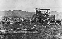 A steam-tractor in a field. Three men stand beside the machine.