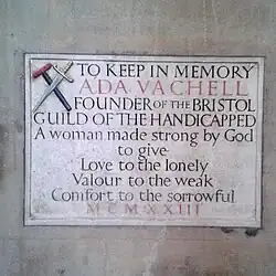 Engraved plaque. At the top left is a crutch crossed by a sword, the symbol of the guild of the handicapped she founded. The plaque reads: A woman made strong by God to give love to the lonely Valour to the weak Comfort to the sorrowful