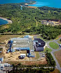 An aerial view of a compound, tree-filled terrain, and blue sea