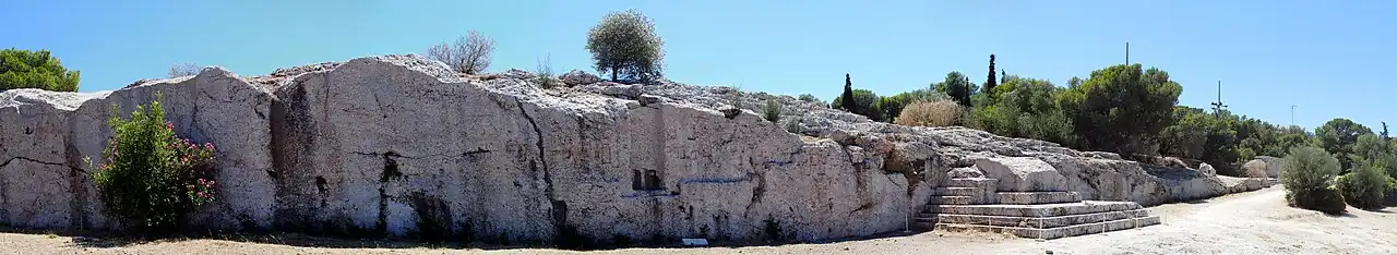 Panorama of the Pnyx, showing the wall with indentations from now-gone wooden beams and the carved steps on the right-hand side.