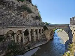Stone Roman arch bridge crossing a narrow river gorge at Vaison-la-Romaine, photographed from the side to show its arches and rock face.