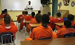 Juveniles in orange jump suits sitting at desks.