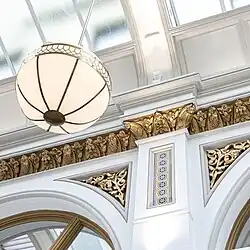 Close-up photograph of a black Victorian-style bollard in the centre of the arcade walkway. A semi-circular mosaic on the floor spells out the letters "Queen's Arcade" around the bollard.