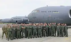 A group of people wearing overalls standing together in front of three grey aircraft are visible in the background.