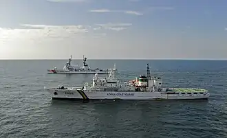 A Korea Coast Guard vessel training with a US Coast Guard vessel, in the distance