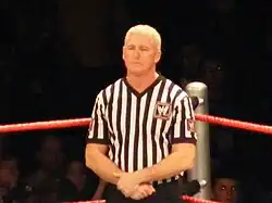 Half-length shot of Armstrong in a striped referee shirt, standing in a wrestling ring