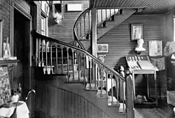 A black-and-white image of the curving wooden staircase with Gothic-arched banister described in the accompanying text. There are many artifacts, paintings and other decorations on the walls