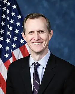 Official House portrait of Whitesides smiling in front of the U.S. flag, wearing a black suit, light blue shirt, and striped dark red and blue tie.