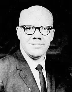 A black-and-white headshot of Douglas in glasses, wearing a suit